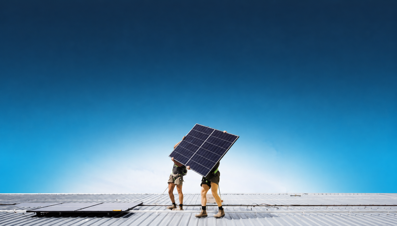 Two Lenergy installers lifting a solar panel into place on a rooftop